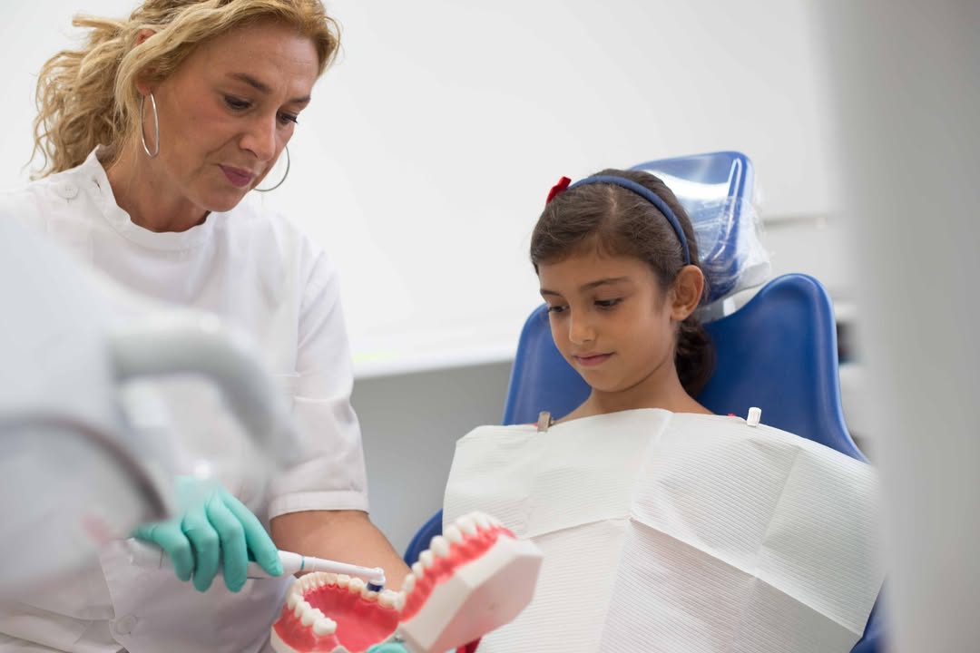 Dentista mostra a una giovane paziente come prendersi cura dei denti